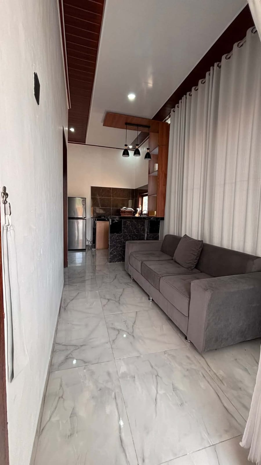 Furnished sitting area with grey sofa leading towards the kitchen in Lombok Stay 31